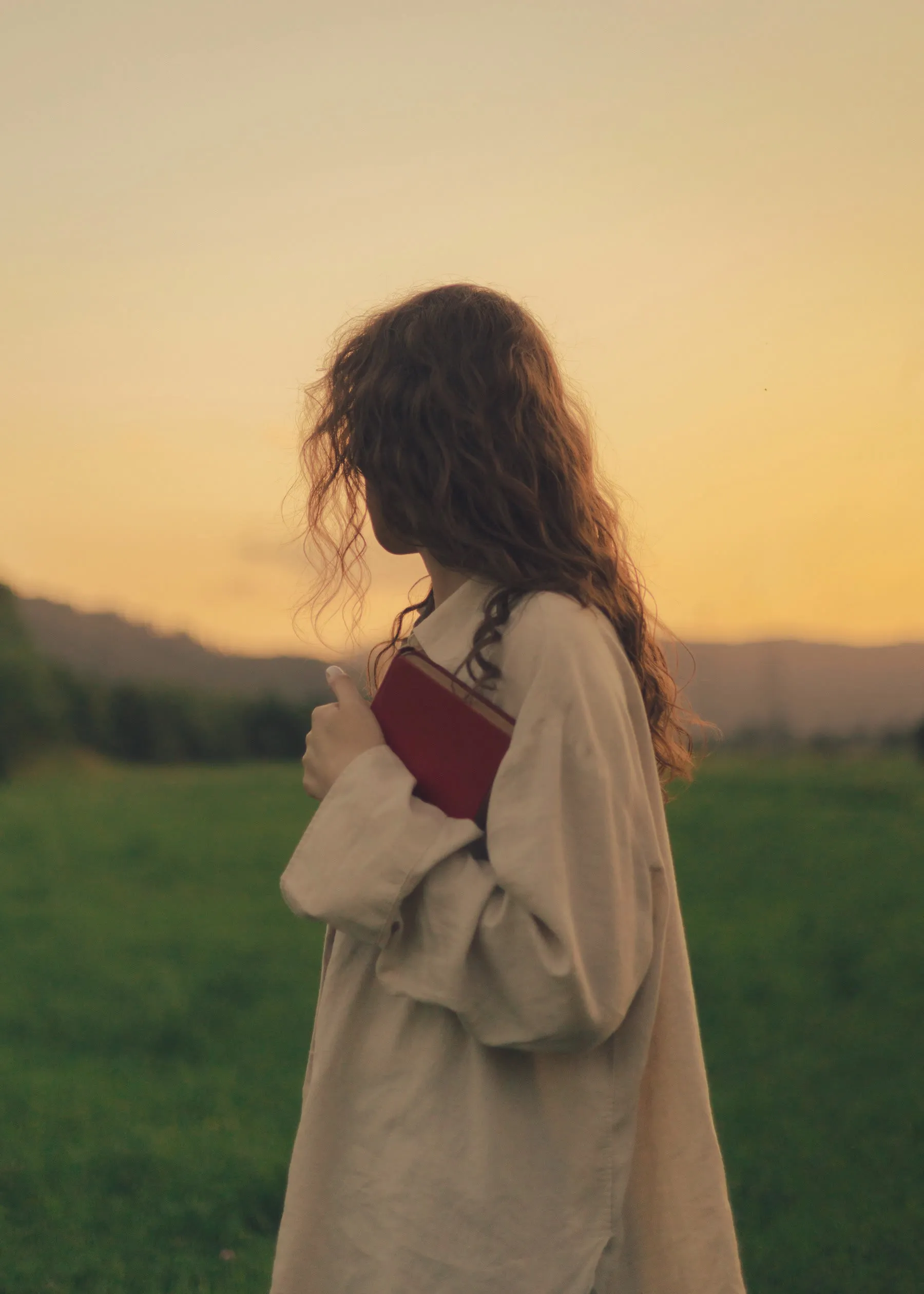 A person holding a red book standing in a field at sunset