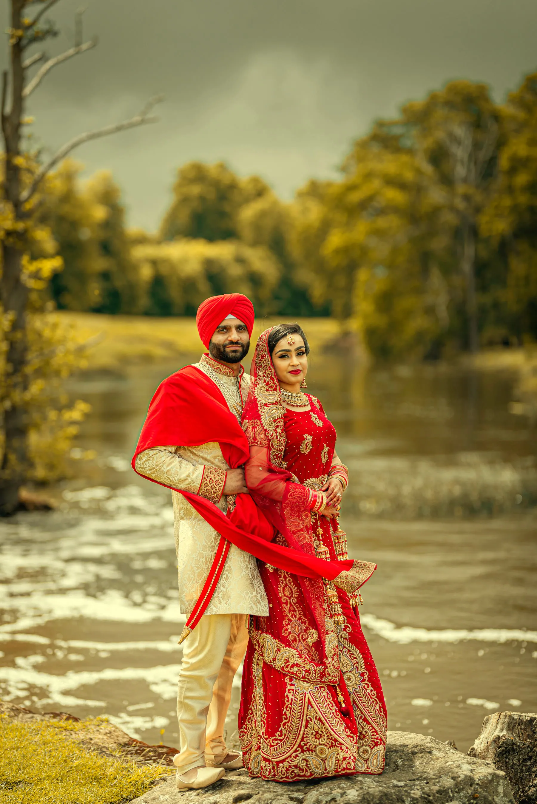 A couple in red and gold wedding dress standing by water