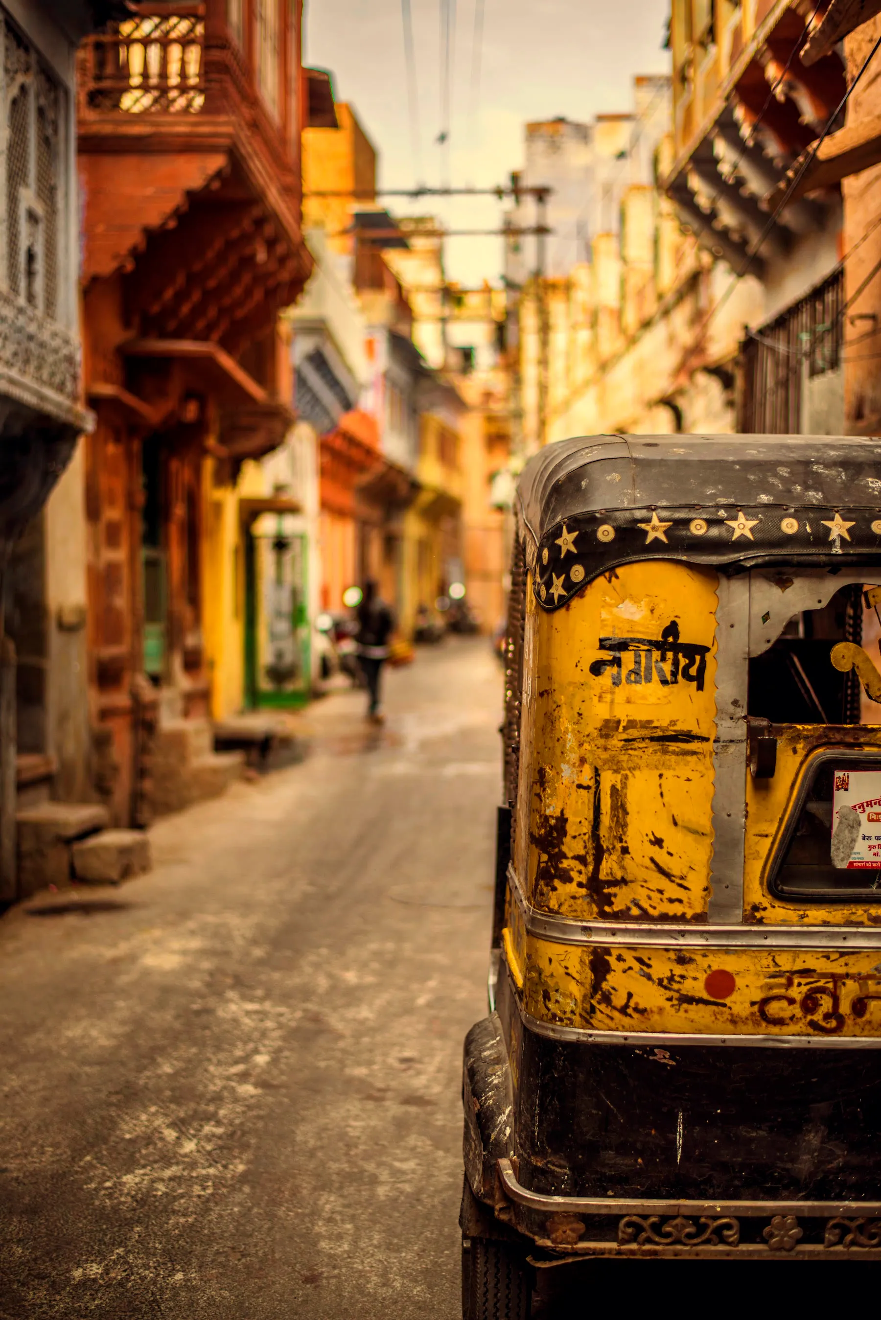 A yellow auto rickshaw parked on a narrow painted street